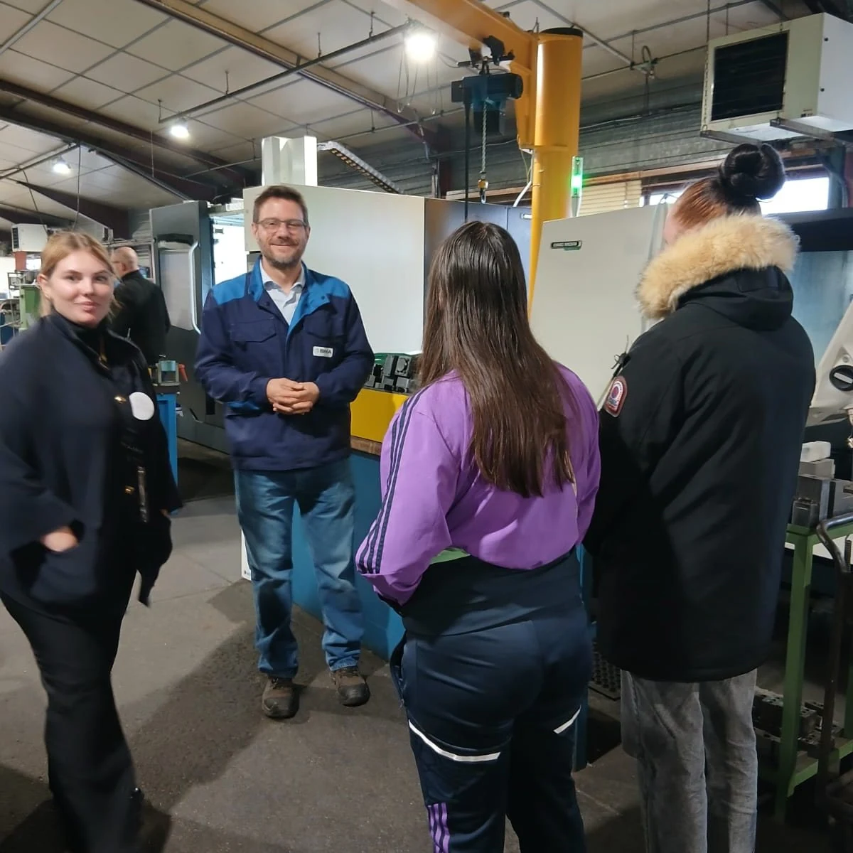 Des participants échangent avec un professionnel dans un atelier industriel.